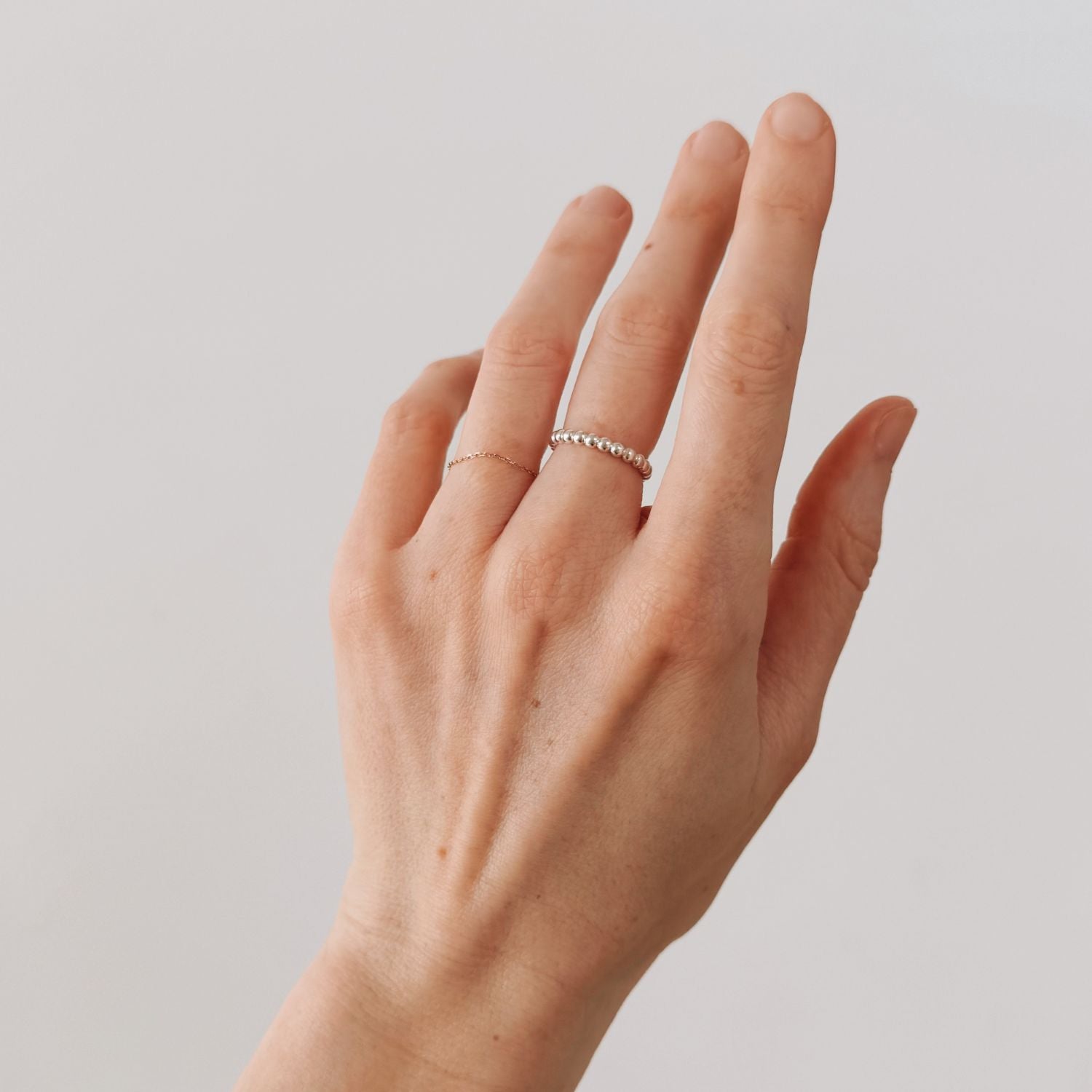 Hand wearing two rings on a plain background