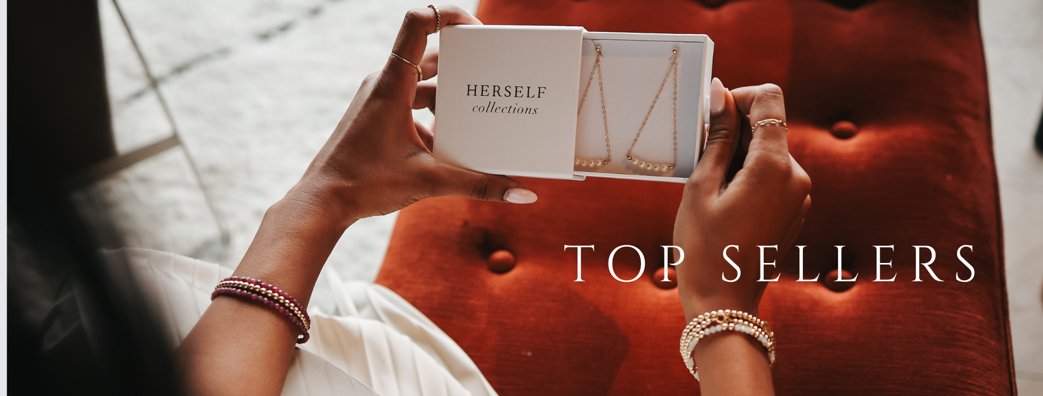 Person holding a product box with jewelry on a red cushion, labeled 'Top Sellers'.
