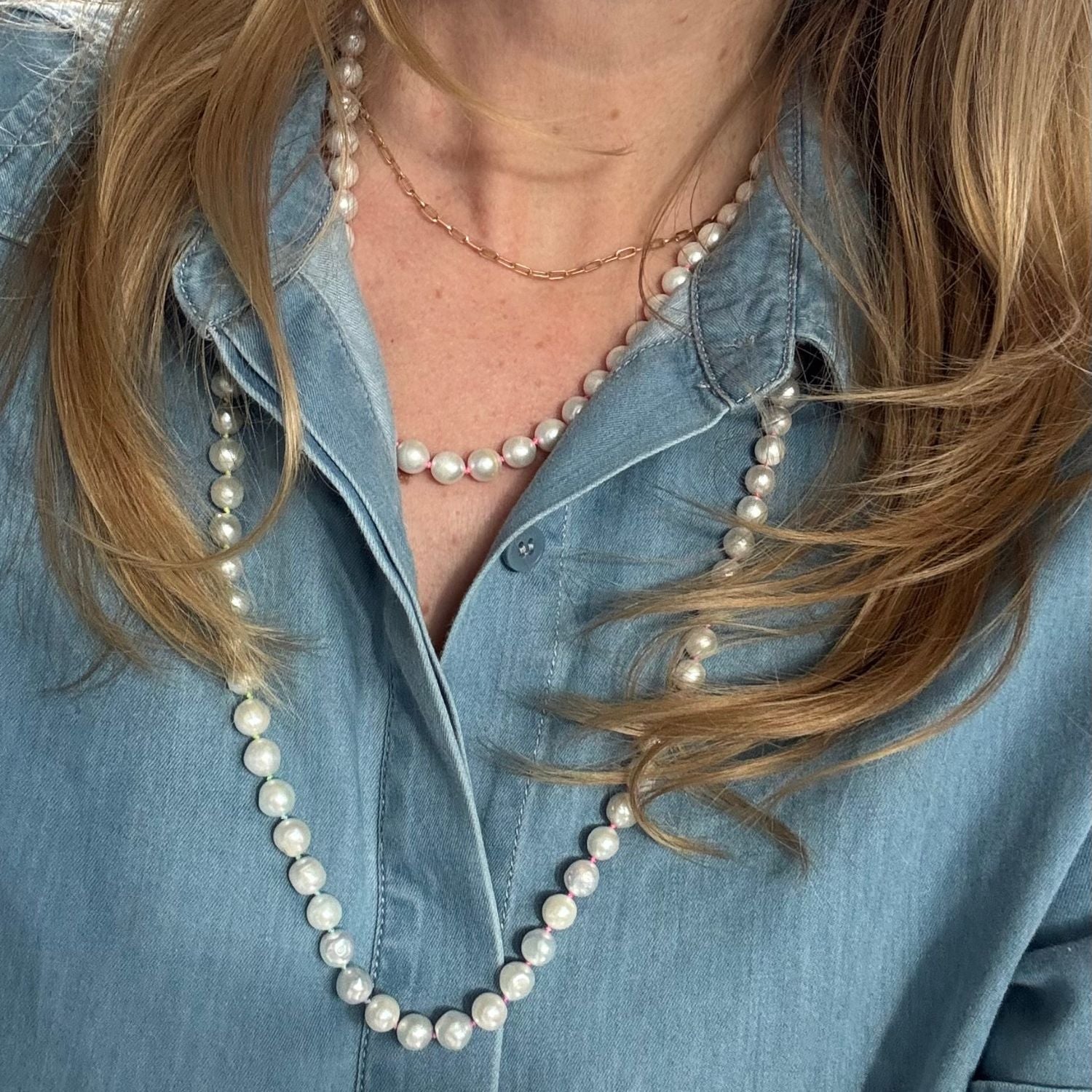 Person wearing a long pearl necklace with a denim shirt