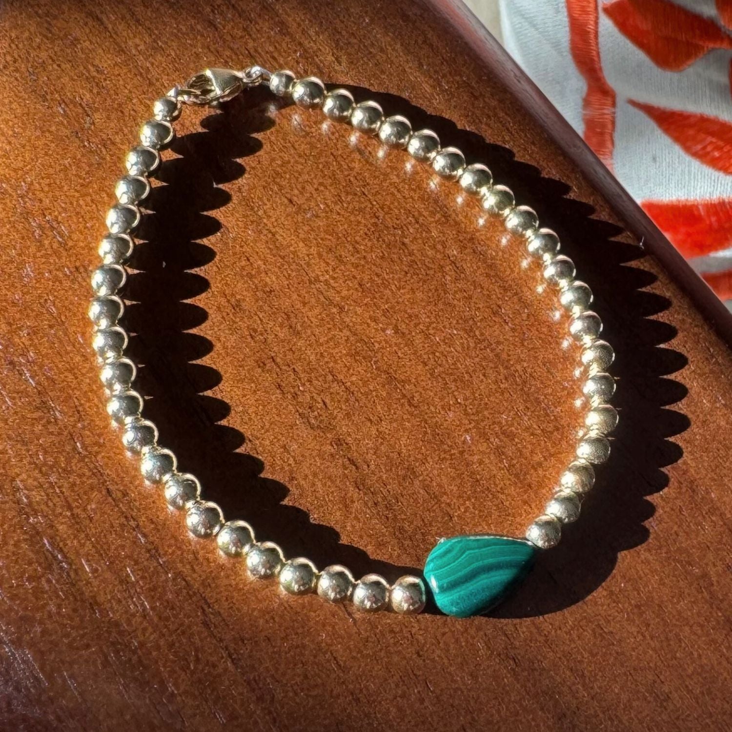 gold bead bracelet with a green teardrop malachite center stone on a wooden backdrop