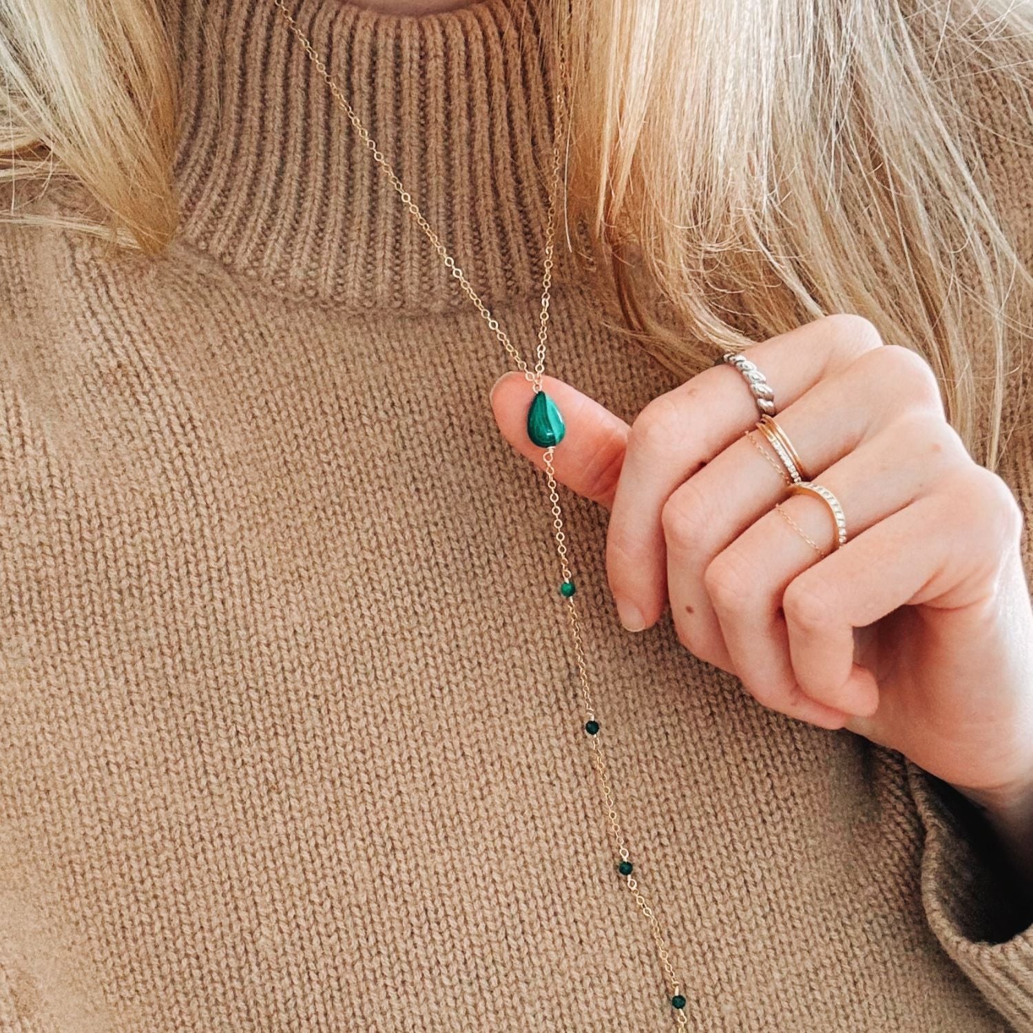 Close-up of a hand wearing a necklace with green beads and rings on a beige sweater background