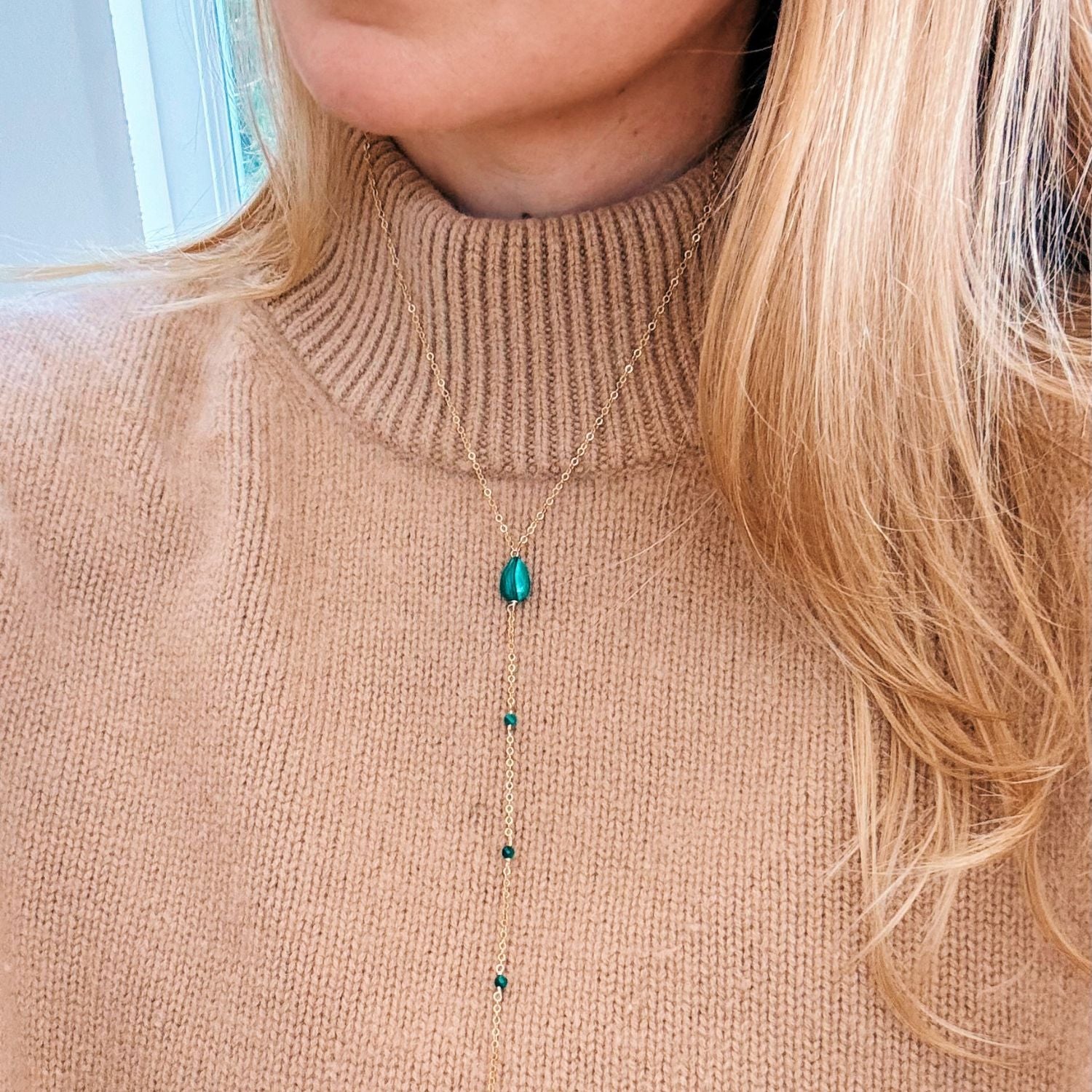 Person wearing a beige sweater with a necklace featuring malachite beads.