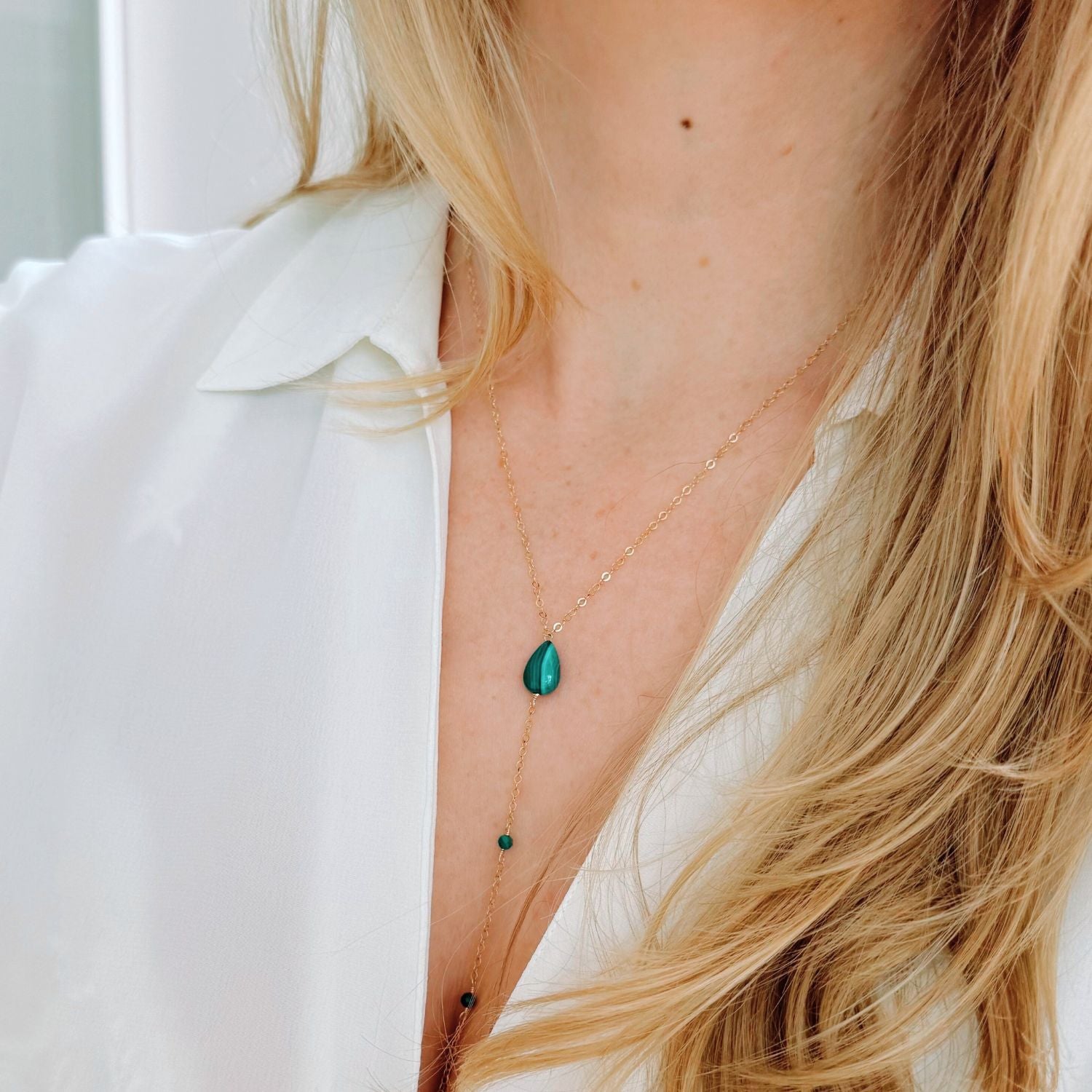Necklace with a green teardrop pendant worn by a person with blonde hair.