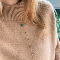 Person wearing a beige sweater with a necklace featuring green beads.