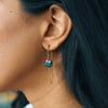 Close-up of an ear wearing a green gemstone earring with gold chain.