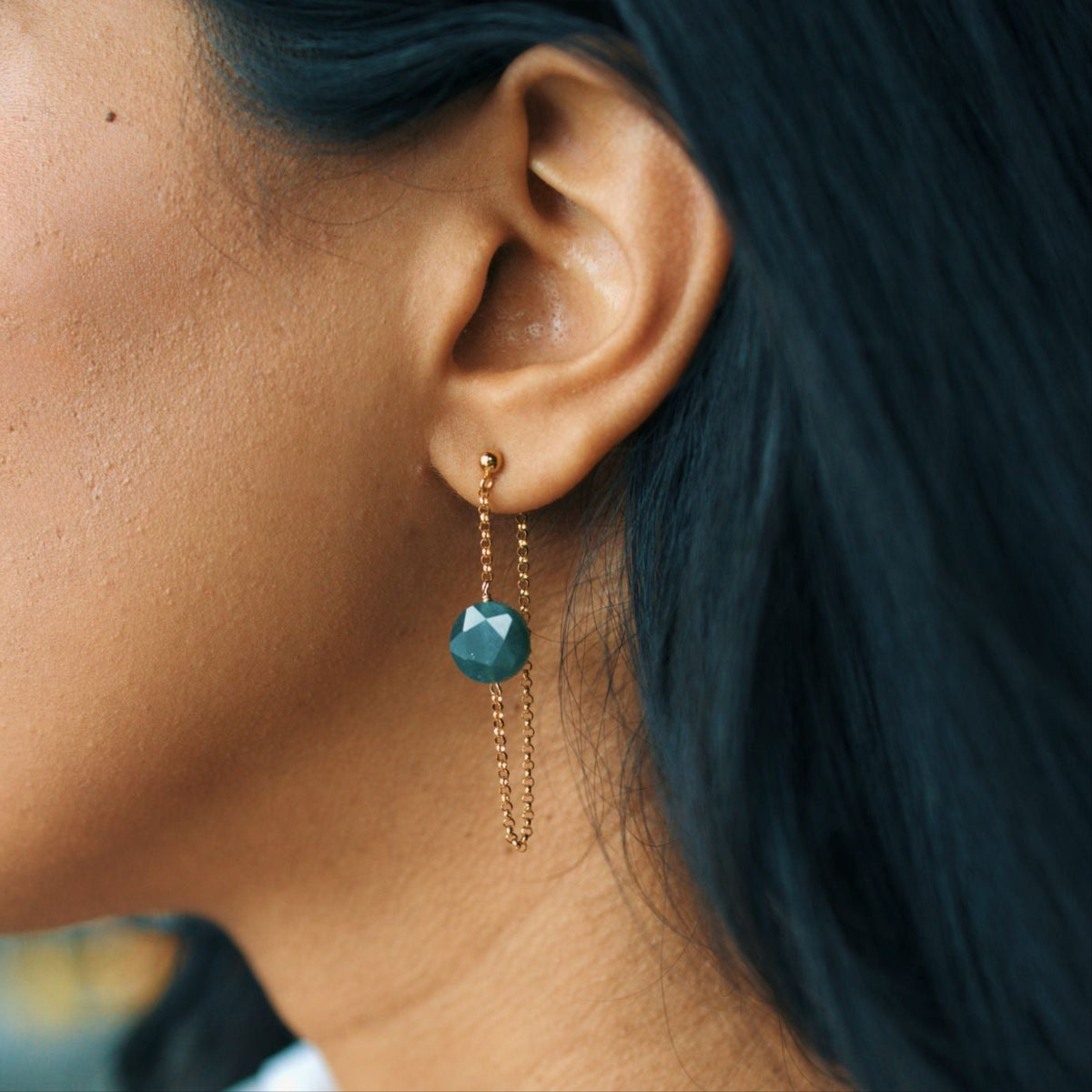 Close-up of an ear wearing a green gemstone earring with gold chain.