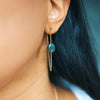 Gold chain earring with a green gemstone worn by a person with dark hair.
