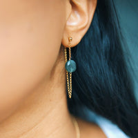 Gold chain earring with a green gemstone worn by a person with dark hair.