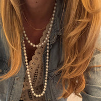Person wearing a long pearl necklace with denim jacket and lace top