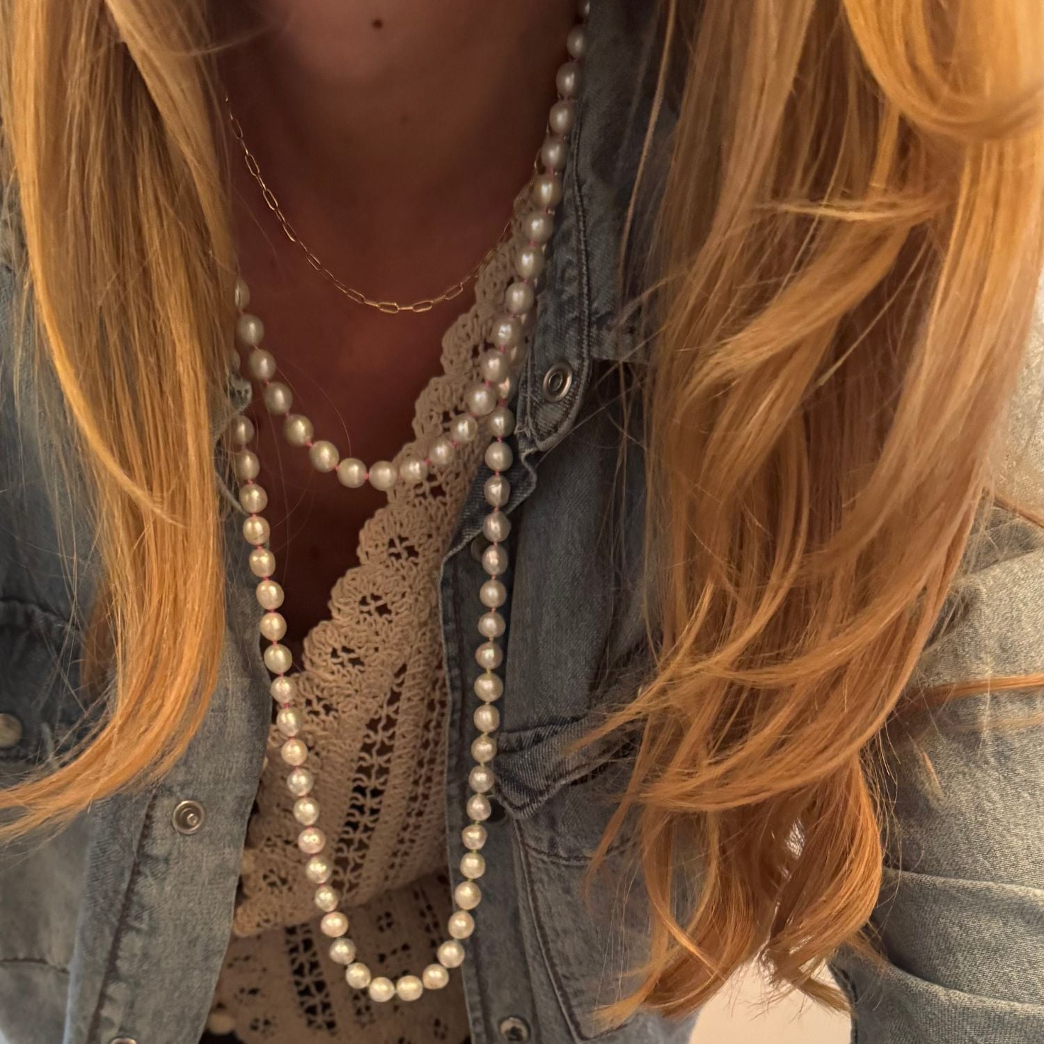 Person wearing a long pearl necklace with denim jacket and lace top
