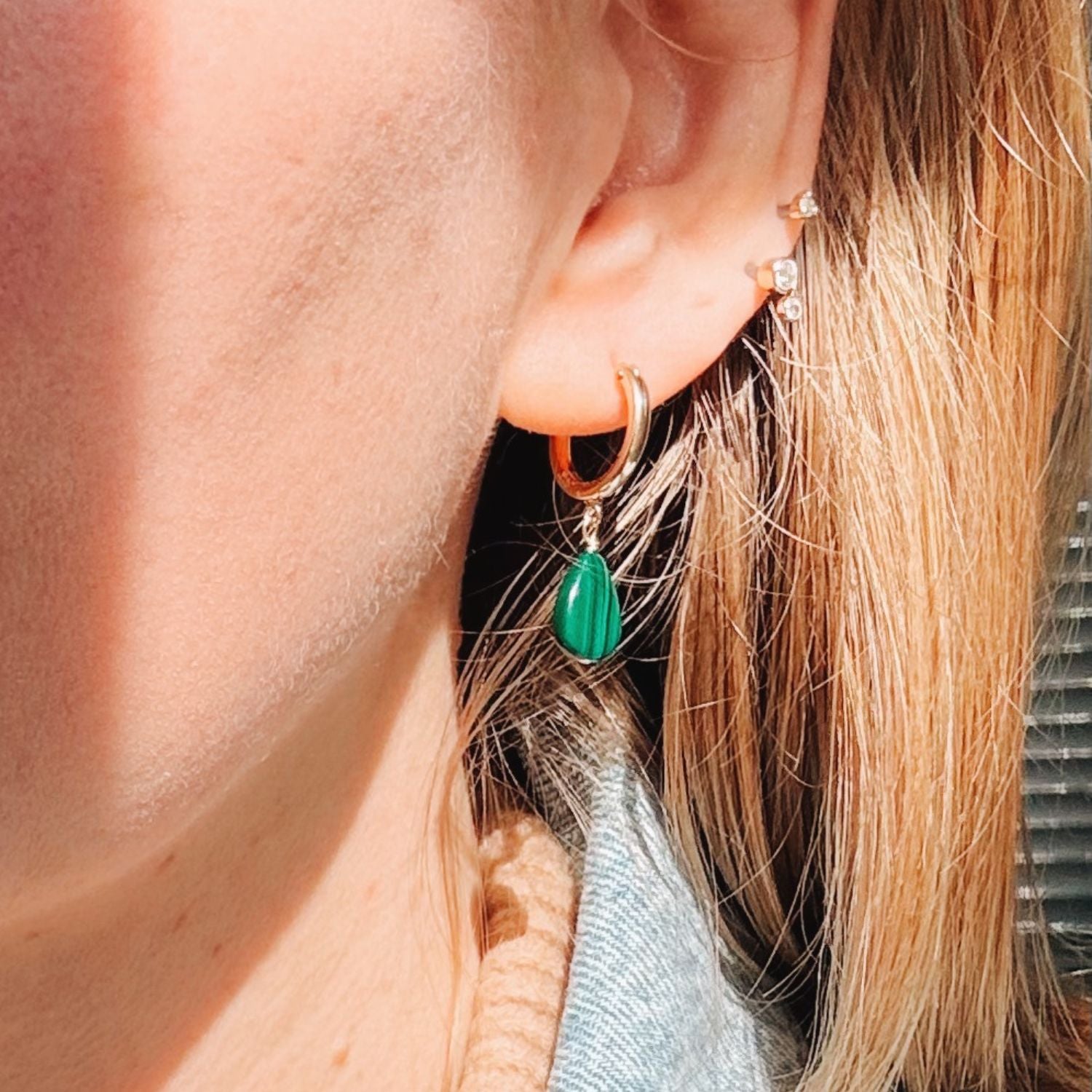 Close-up of an ear wearing a gold hoop earring with a green teardrop pendant.