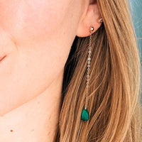 Close-up of a person wearing a gold earring with a green gemstone.