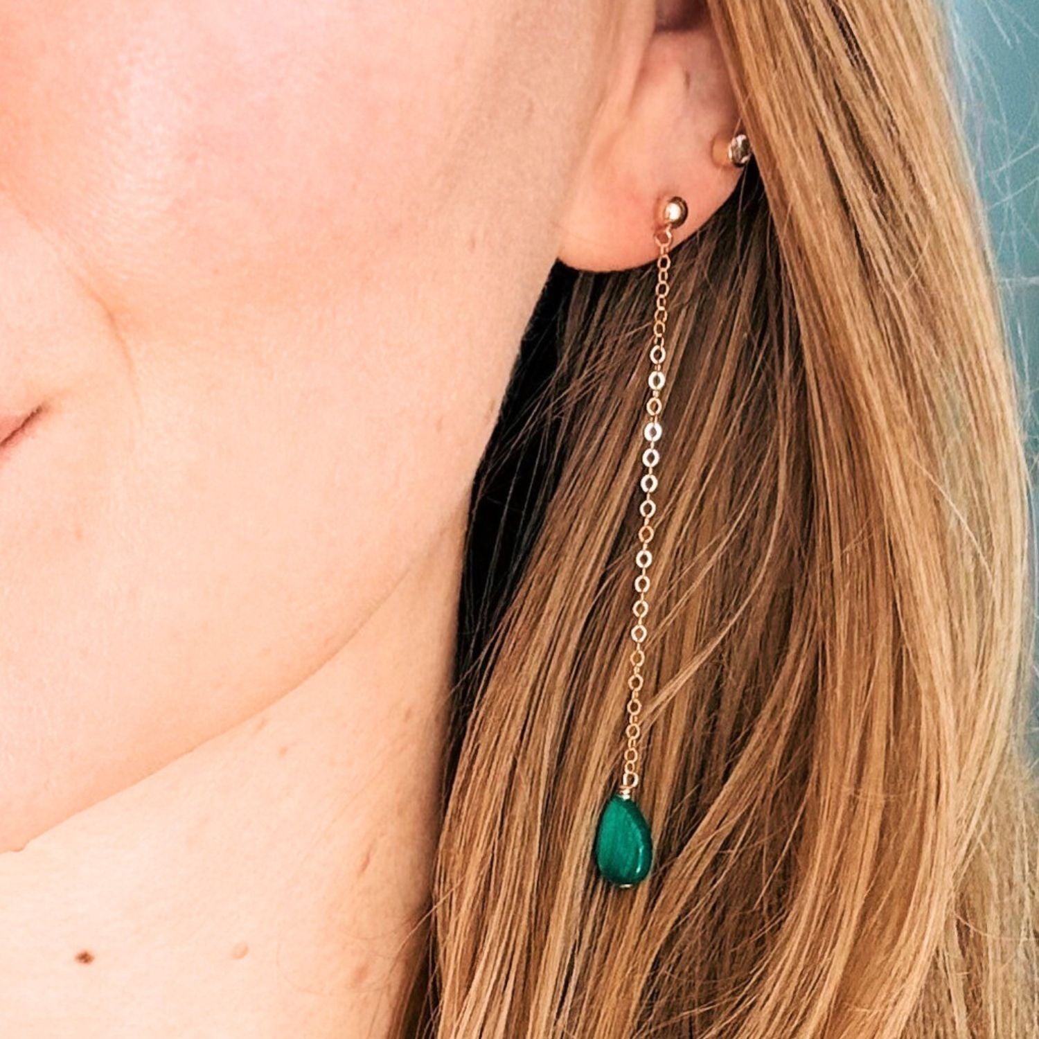 Close-up of a person wearing a gold earring with a green gemstone.