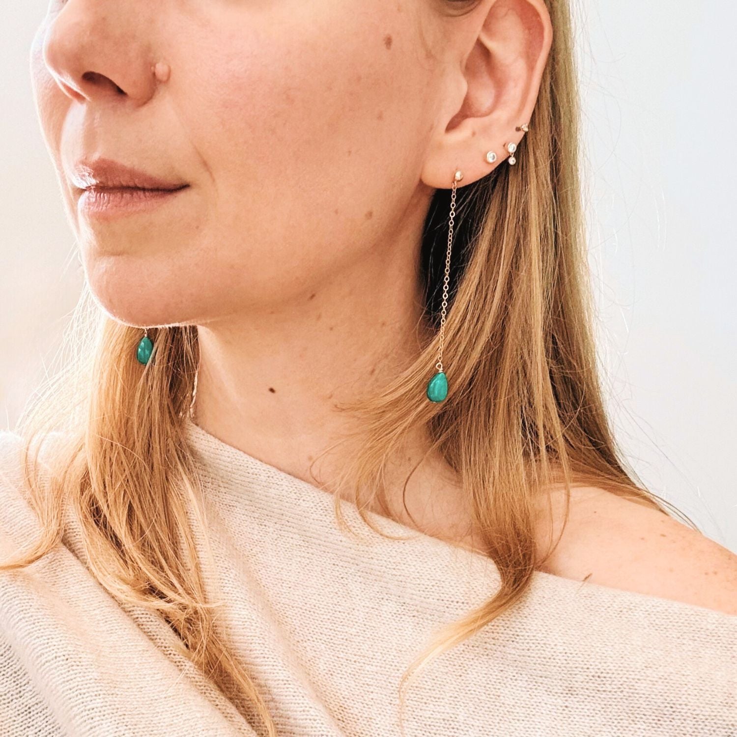 Close-up of a woman wearing malachite earrings with a plain background