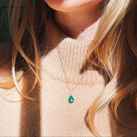 Close-up of a person wearing a necklace with a green malachite teardrop pendant.