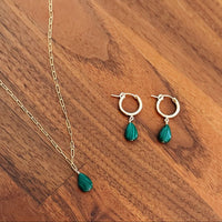 Jewelry set with gold chain and green teardrop pendants on a wooden surface