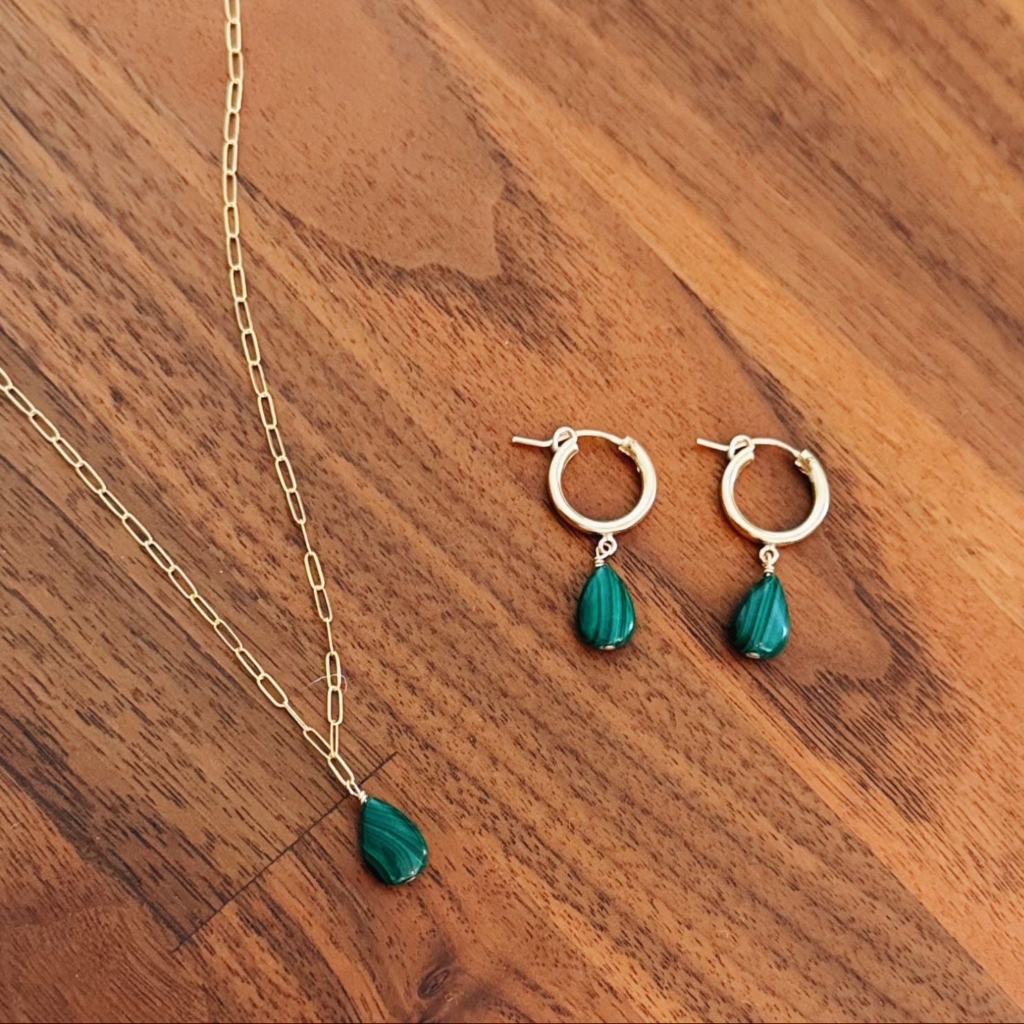 Jewelry set with gold chain and green teardrop pendants on a wooden surface