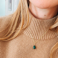 Person wearing a beige sweater with a green teardrop pendant necklace.