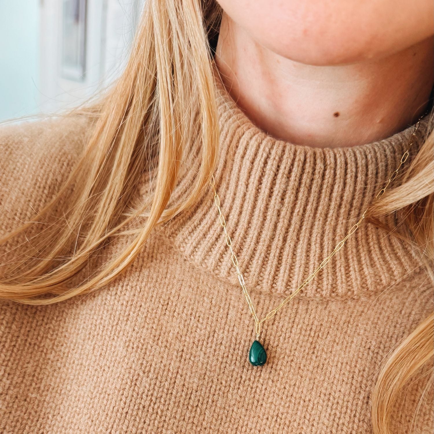 Person wearing a beige sweater with a green teardrop pendant necklace.