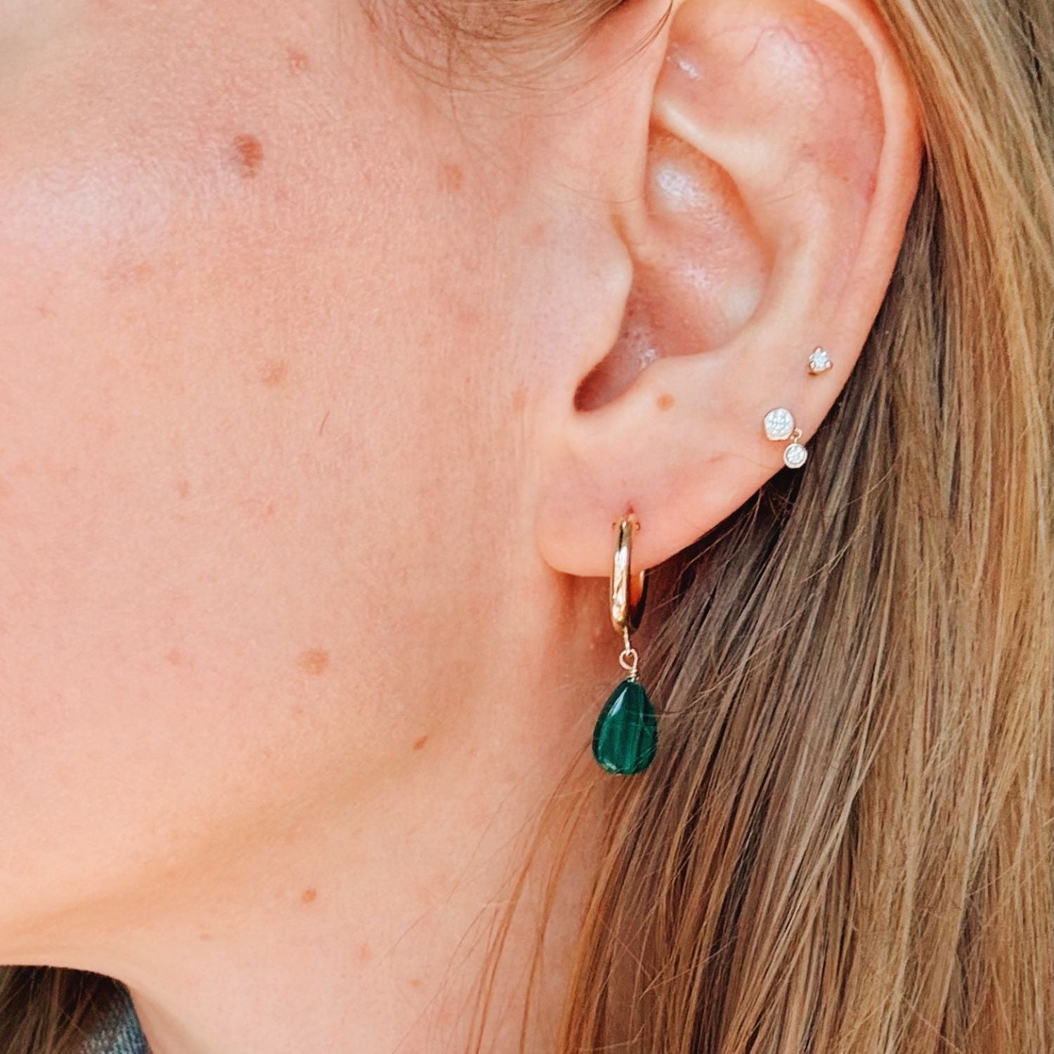 Close-up of an ear with gold hoop earrings and green malachite teardrop earrings.