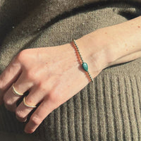 a woman's hand featuring a gold bead bracelet with a green malachite center stone set against a brown knit 