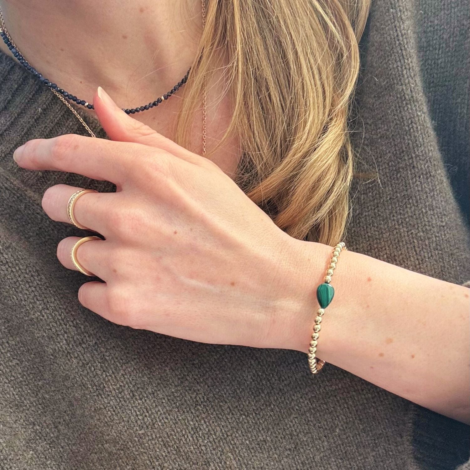 a woman's hand featuring a gold bead bracelet with a green malachite center stone 