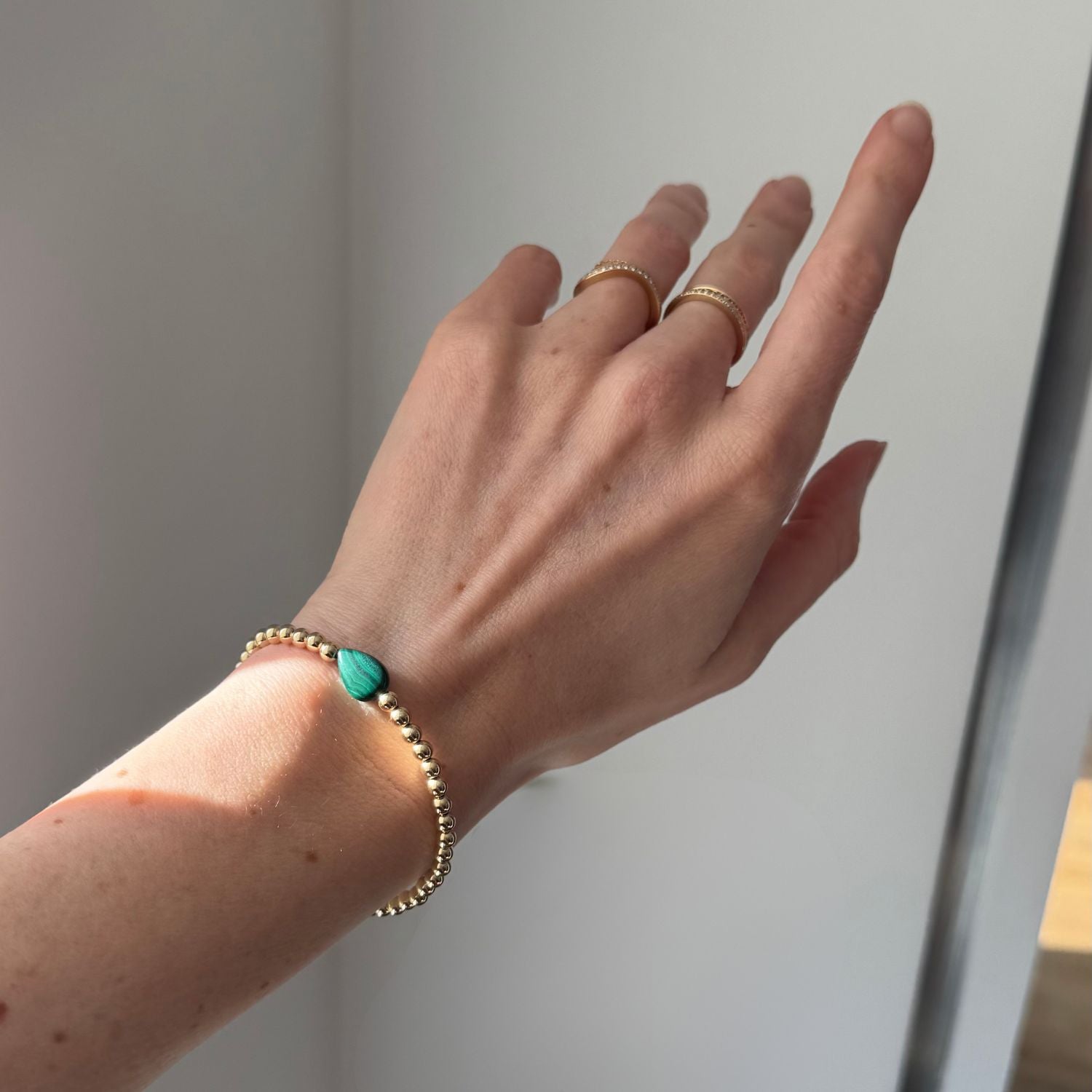 a woman's hand featuring a gold bead bracelet with a green malachite center stone